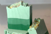 Ombre Green layers of colored bars of soap stacked on top of each other with a bar leaning on the stack. This is the Soft Eucalyptus soap.