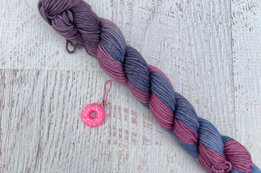 A mini Skein of Hand Dyed Merino Sock Weight Yarn and a coordinating stitch marker. Suitable for knitting and crocheting 