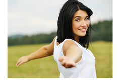 a female with black hair and green eyes is smiling and has arms spread open in a T-position. She seems happy.