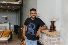 A man leaning against a shelf wearing a black Harry Potter Tshirt with a Raven making the shape of an R.