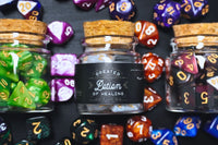 Three glass corked bottles with a black label that says Greater Potion of healing with different colored TTRPG and D&D dice.