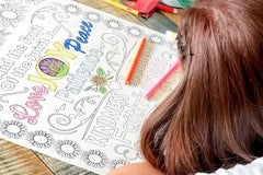 Young lady coloring an 18"x24" coloring page with Love, Joy, Peace, Patience, Kindness, Faithfulness printed on it. Pink, Yellow, and Blue.