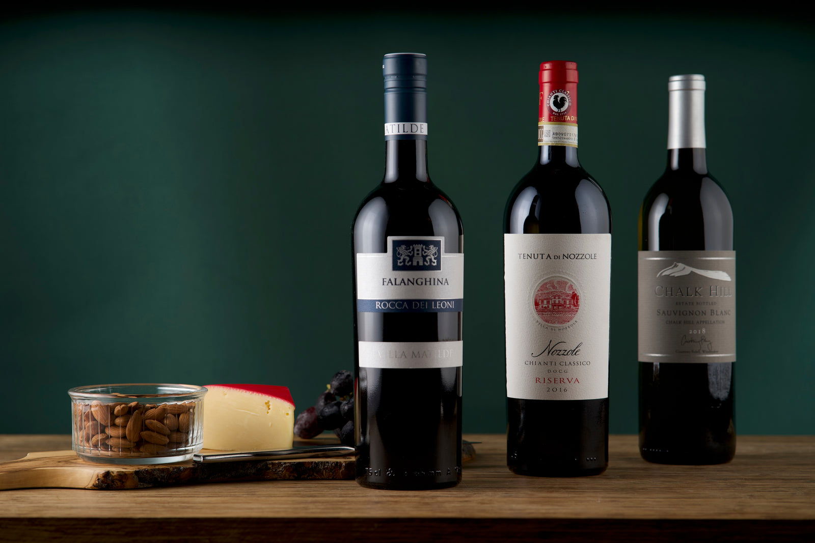 3 bottles of wine next to a board with almonds, cheese and grapes, from a The Standard - Wine Club subscription box.