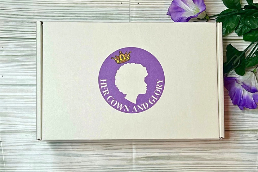 Her Crown and Glory subscription box against wooden-style background placed next to purple flowers  