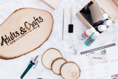 Items from the Adults and Crafts subscription box including slices of wood, wood burning tools and paints.