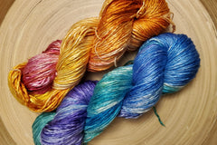 Two Skeins of Hand Dyed Silk Yarn in Worsted Weight. One is orange and pink and the other is blue purple and teal 