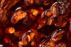 A blown up shot showing the crunchy and delicious flavors of chili crisp, floating around in oil. Garlic and chilis for days