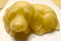 An ivory-colored lotion bar shaped like a sleeping puppy with long, floppy ears rests on a white base.