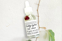 The Buddy System Face Serum by Greenmade goods showing a rose bud in the bottle with concrete and a vine in the background.