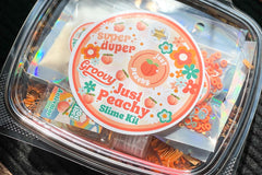 Just Peachy groovy slime kit from Bored to Brilliant in a clear deli container with glitter and clay pieces, slime activator, jello powder.
