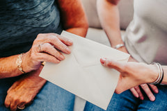a young female handing an envelope with a greeting card inside to an older female woman to receive and open