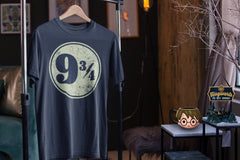 A dark blue tshirt with the iconic Platform 9 3/4 design hanging on a hanger on a rack. A Harry Potter 3D mug is next to it.