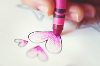 Young lady's hand close up with a magenta crayon coloring a few hearts on a coloring page. Relaxing with coloring.