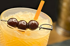 A close up of a Three Dots and A Splash cocktail. This picture shows the orange of the drink in contrast to the deep red of cherries.