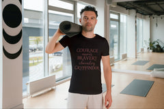 A man in a yoga studio carrying a yoga mat and wearing a tshirt inspired by Harry Potter with words like Courage, Bravery, and Gryffindor.