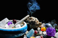 black background with a jumbled mix of all colors of crystals. a bowl is on the left filled with crystals and smoke wafting off of incense