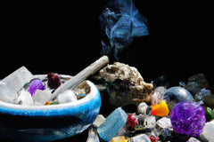 black background with a jumbled mix of all colors of crystals. a bowl is on the left filled with crystals and smoke wafting off of incense