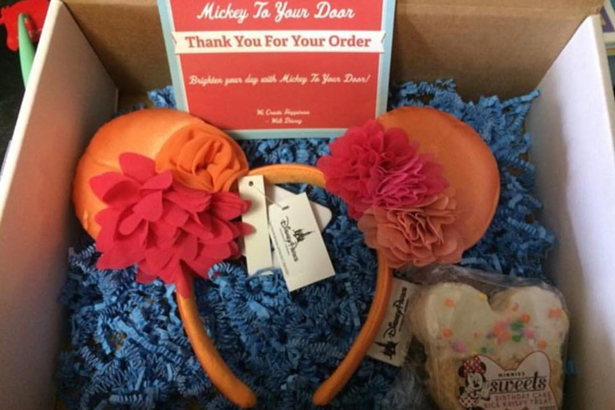 A Mickey to Your Door subscription box filled with an orange and red Mickey ears headband and a Mickey Mouse cake.
