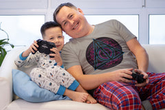 A man and young boy playing video games. The man is wearing a Deathly Hallows Tshirt with a Triangle design.